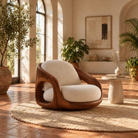 Barrel shaped wood chair with oval side openings and cream cushions in a bright living room with arched windows and plants