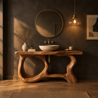 Freestanding vanity base with looping open legs and a thick wood slab top in a dark bathroom at golden hour