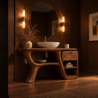Freeform vanity cabinet with a swooping leg and a small drawer above open cubbies in an evening bathroom with walnut wall paneling