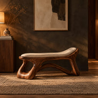 Sculpted bench with a cushioned seat and open loop legs in a dark entryway at golden hour
