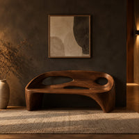 Sculpted bench with a cutout back and swept side legs in a dark entryway at golden hour