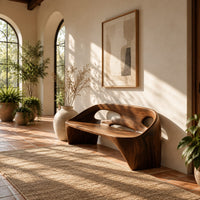 Sculpted bench with a cutout back and swept side legs in a bright entryway with arched windows and plants