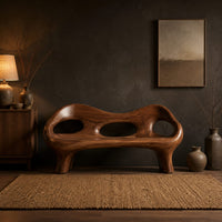 Sculpted wood bench with a low back and three oval openings in a dark entryway at golden hour