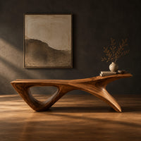 Long low wooden bench with a triangular open leg and a swept tapered end in a dark studio against a charcoal plaster wall