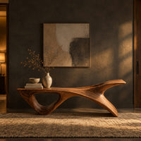 Long low wooden bench with a triangular open leg and a swept tapered end in a dark entryway at golden hour