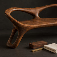 Corner detail of wood bench with two oval back openings and looped legs beside wood, brass and linen samples