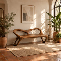 Wood bench with two oval back openings and looped legs in a bright entryway with arched windows and plants
