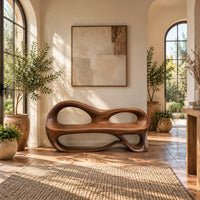 Bench with a sculpted back that has two oval openings in a bright entryway with arched windows and plants