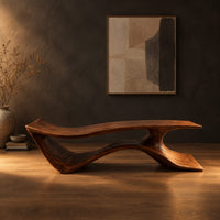 Long low bench with a wave shaped plank seat on a swept base in a dark studio against a charcoal plaster wall