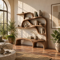 Sculpted bookshelf with an integrated bench seat and open shelves in a bright living room with arched windows and plants