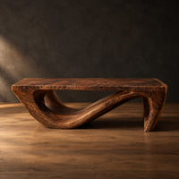 Rectangular coffee table with a thick top over a swooping open loop base in a dark studio against a charcoal plaster wall