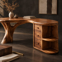 Corner detail of kidney shaped wood desk with a tree trunk leg and a drawer pedestal beside wood, brass and linen samples