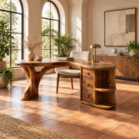 Kidney shaped wood desk with a tree trunk leg and a drawer pedestal in a bright home office with arched windows and plants