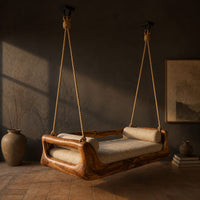 Hanging daybed swing with a sculpted wood frame and a cushioned seat, three-quarter view showing the grain