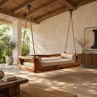 Hanging daybed swing with a sculpted wood frame and a cushioned seat in a bright open plan porch