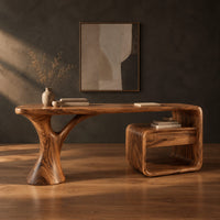 Sculpted desk with a tree trunk leg and a loop frame side unit in a dark studio against a charcoal plaster wall