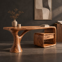 Corner detail of sculpted desk with a tree trunk leg and a loop frame side unit beside wood, brass and linen samples
