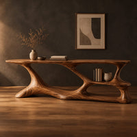Long desk on a freeform sculpted base with open loops and a small shelf in a dark studio against a charcoal plaster wall