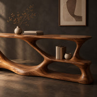 Corner detail of long desk on a freeform sculpted base with open loops and a small shelf beside wood, brass and linen samples