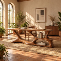 Long desk on a freeform sculpted base with open loops and a small shelf in a bright home office with arched windows and plants