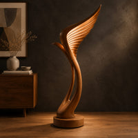 Tall floor lamp shaped like a ribbed feather wing on a round wooden base in a dark studio against a charcoal plaster wall