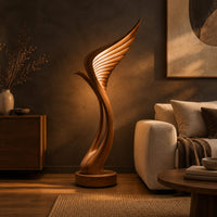 Tall floor lamp shaped like a ribbed feather wing on a round wooden base in a dark living room at golden hour