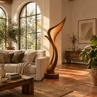 Tall floor lamp shaped like a ribbed feather wing on a round wooden base in a bright living room with arched windows and plants