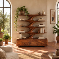 Bookshelf with sculpted flared tiers on a low base with three front panels in a bright living room with arched windows and plants