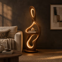 Sculpted floor lamp with glowing oval cutouts and a mid level shelf in a dark living room at golden hour