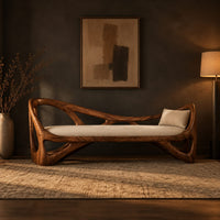 Sculpted wooden bench with open branching sides and a padded seat in a dark entryway at golden hour