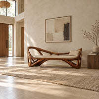 Sculpted wooden bench with open branching sides and a padded seat in a bright open plan entryway
