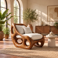 Lounge chair with circular side cutouts and a high back with cream cushions in a bright living room with arched windows and plants