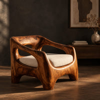 Sculpted wooden lounge chair with open arm cutouts and a cream seat cushion, three-quarter view showing the grain