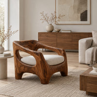 Sculpted wooden lounge chair with open arm cutouts and a cream seat cushion in a Scandinavian living room with white walls
