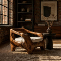 Sculpted wooden lounge chair with open arm cutouts and a cream seat cushion in an industrial loft living room with exposed brick