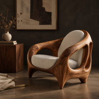 Corner detail of sculpted lounge chair with an open cutout wood frame and cream cushions beside wood, brass and linen samples