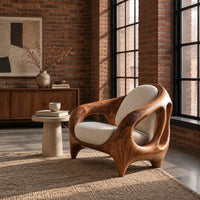 Sculpted lounge chair with an open cutout wood frame and cream cushions in an industrial loft living room with exposed brick
