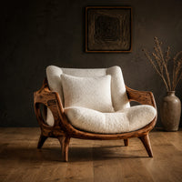 Lounge chair with a sculpted wooden frame and thick cream cushions in a dark studio against a charcoal plaster wall