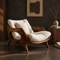 Corner detail of lounge chair with a sculpted wooden frame and thick cream cushions beside wood, brass and linen samples