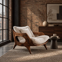 Lounge chair with a sculpted wooden frame and thick cream cushions in an industrial loft living room with exposed brick