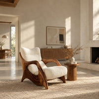 Sculpted wooden lounge chair with open side loops and cream cushions in a bright open plan living room