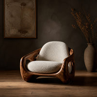 Sculpted lounge chair with oval side cutouts and cream seat cushions in a dark studio against a charcoal plaster wall