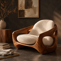 Corner detail of sculpted lounge chair with oval side cutouts and cream seat cushions beside wood, brass and linen samples