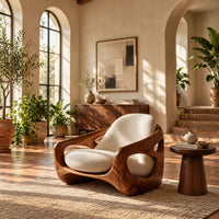 Sculpted lounge chair with oval side cutouts and cream seat cushions in a bright living room with arched windows and plants