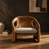 Sculpted wood chair with oval back cutouts and a cushioned seat in a dark studio against a charcoal plaster wall