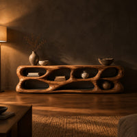 Free form tv stand made of thick sculpted wood with many oval openings in a dark living room at golden hour
