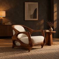 Sculpted lounge chair with an open oval wooden frame and cream cushions in a dark living room at golden hour