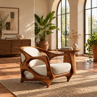 Sculpted lounge chair with an open oval wooden frame and cream cushions in a bright living room with arched windows and plants
