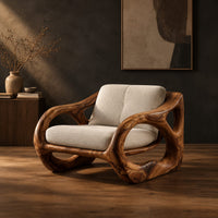 Sculpted wooden armchair with open oval side loops and cream cushions in a dark studio against a charcoal plaster wall