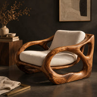 Corner detail of sculpted wooden armchair with open oval side loops and cream cushions beside wood, brass and linen samples